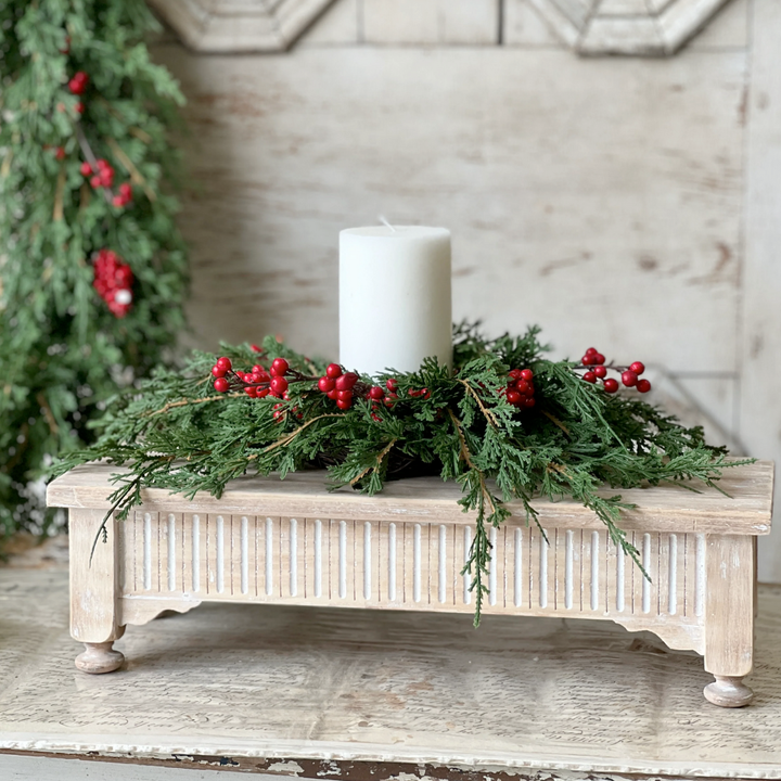 Decorative table centerpiece with greenery, red berries, and a white candle on a wooden surface.