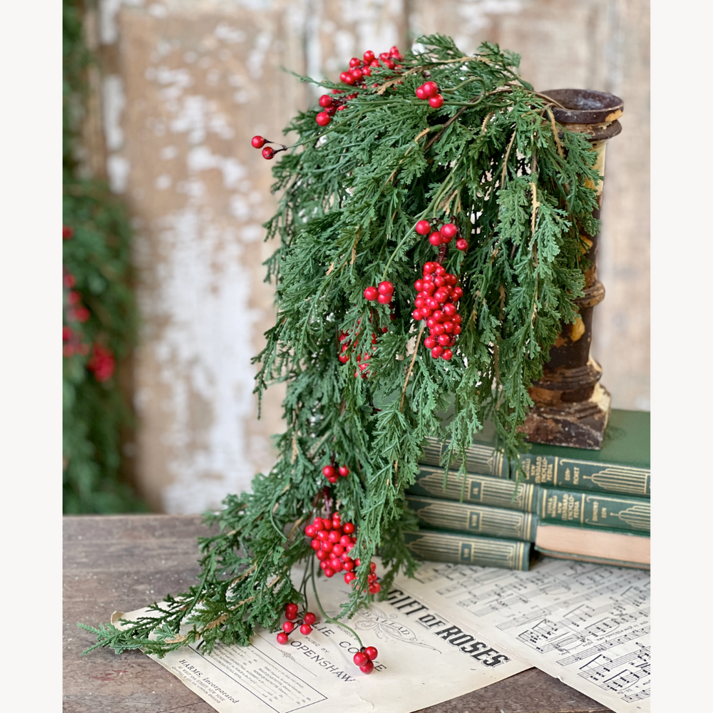 Decorative greenery with red berries on a rustic surface with books and newspaper.