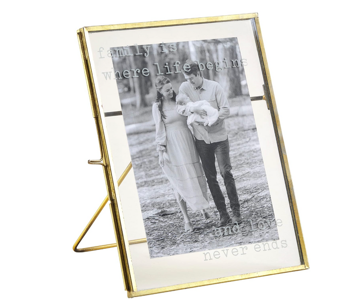 A brass finished metal picture frame with pressed glass panes displaying a photo and the text 'family is where life begins and love never ends'.