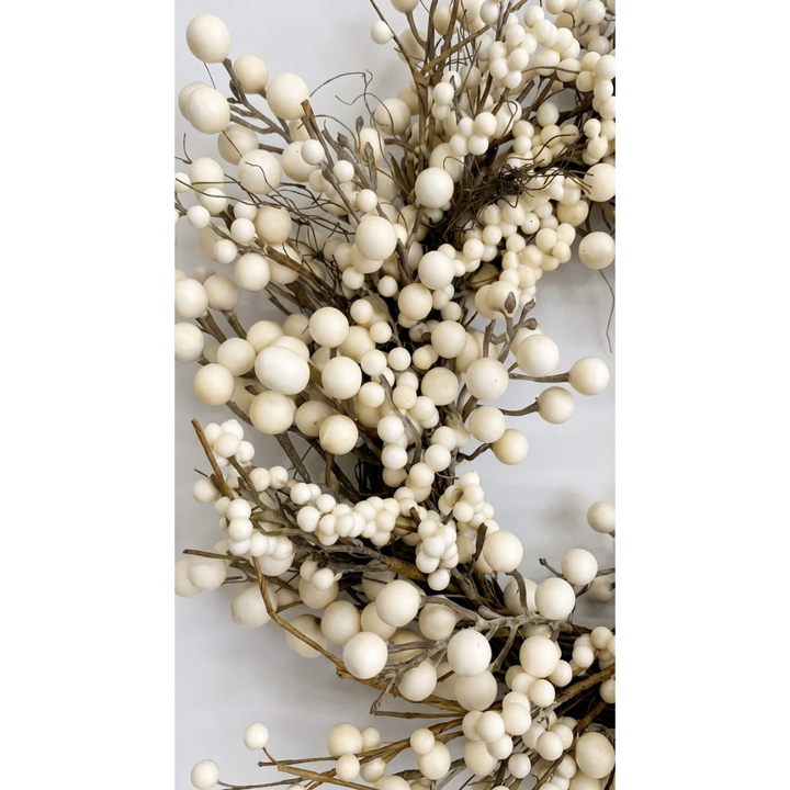 A close-up of a decorative faux berry wreath featuring round off-white berries on a natural brown twig branch, set against a plain light gray background.