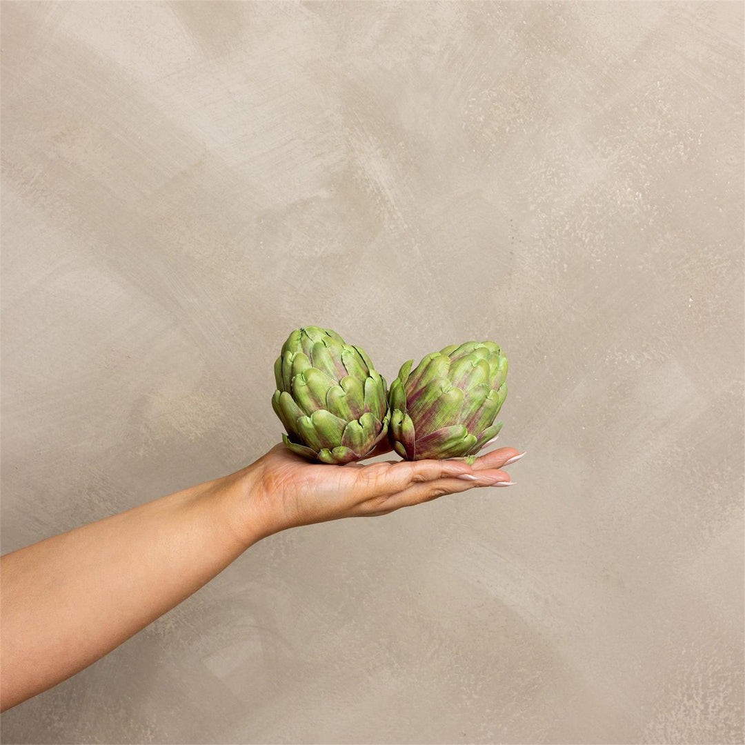 Two artificial artichokes held in a hand against a beige background