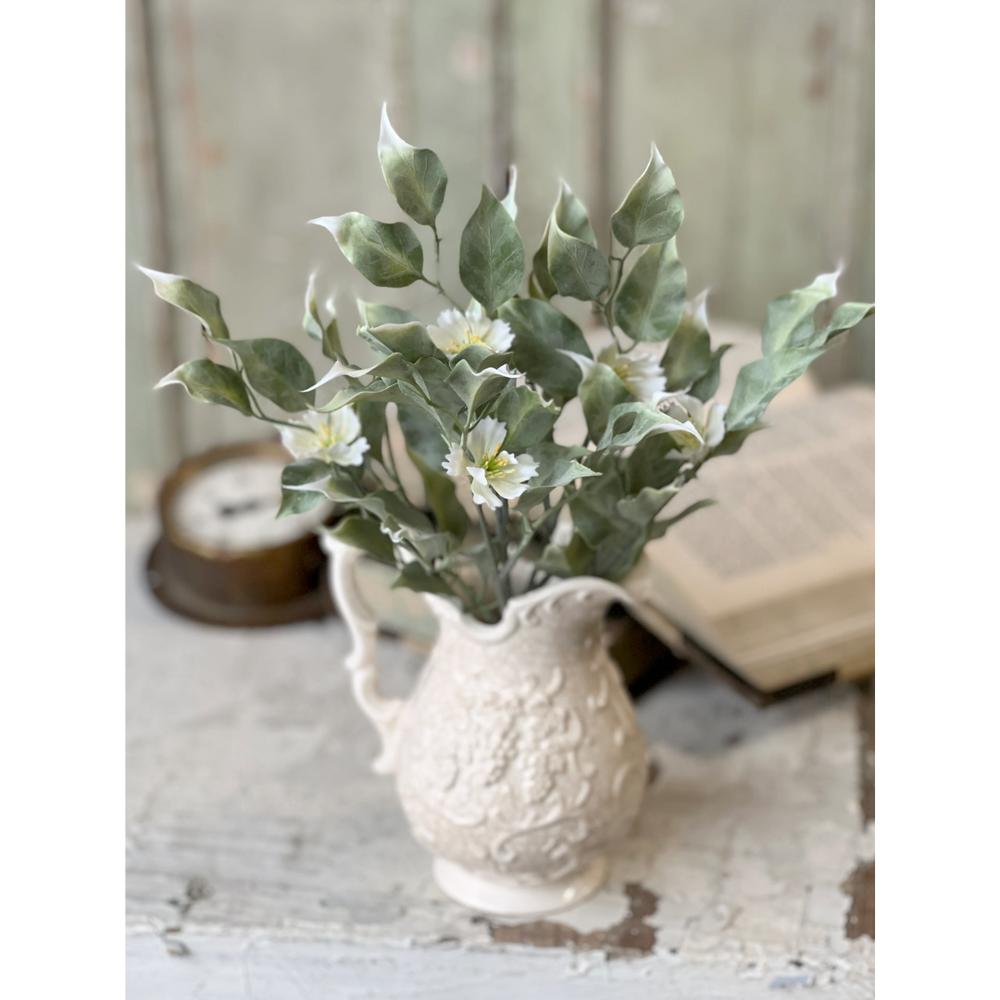 Faux greenery in a decorative white vase on a textured surface with a blurred background