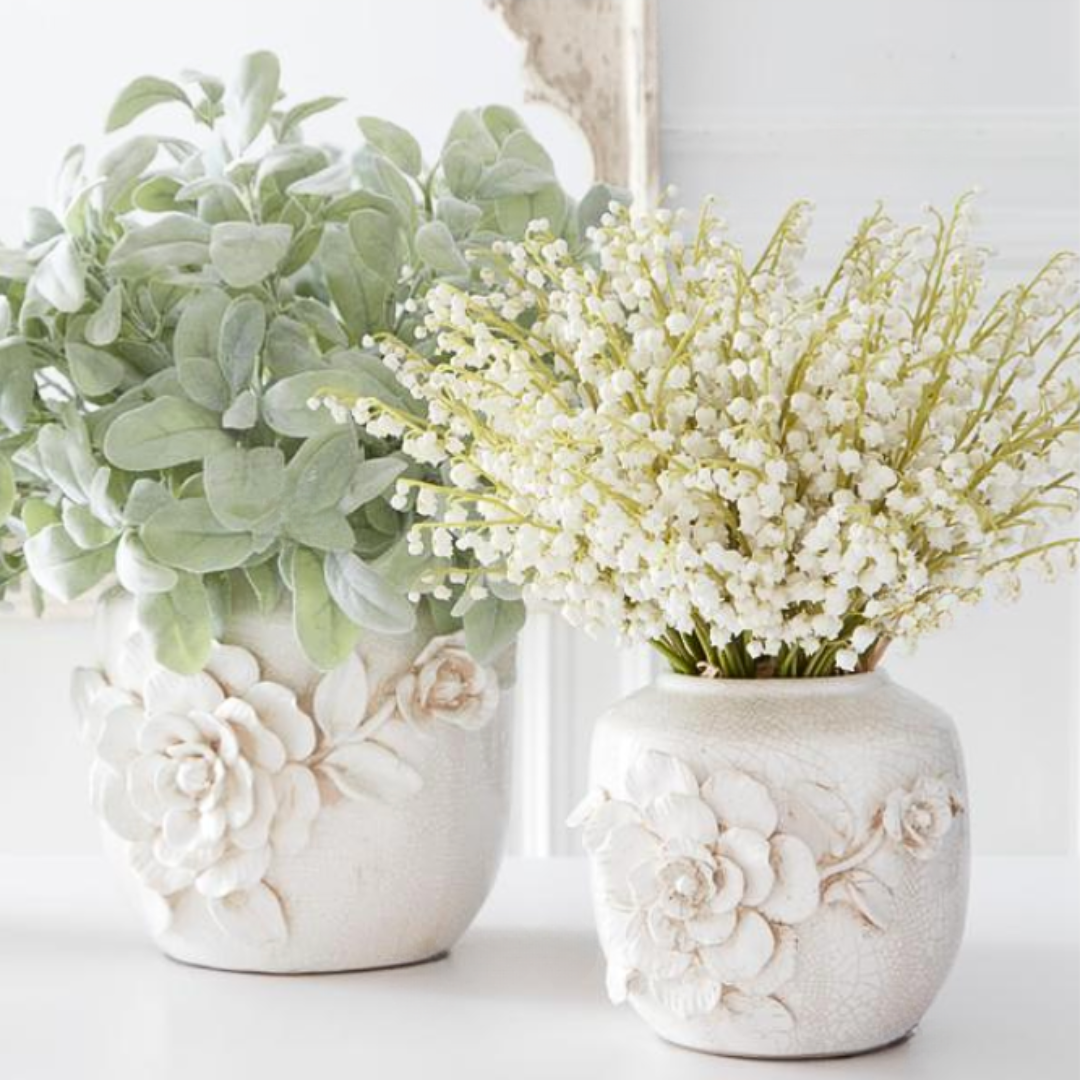 Two decorative vases with floral patterns containing white lily of the valley stems on a white background