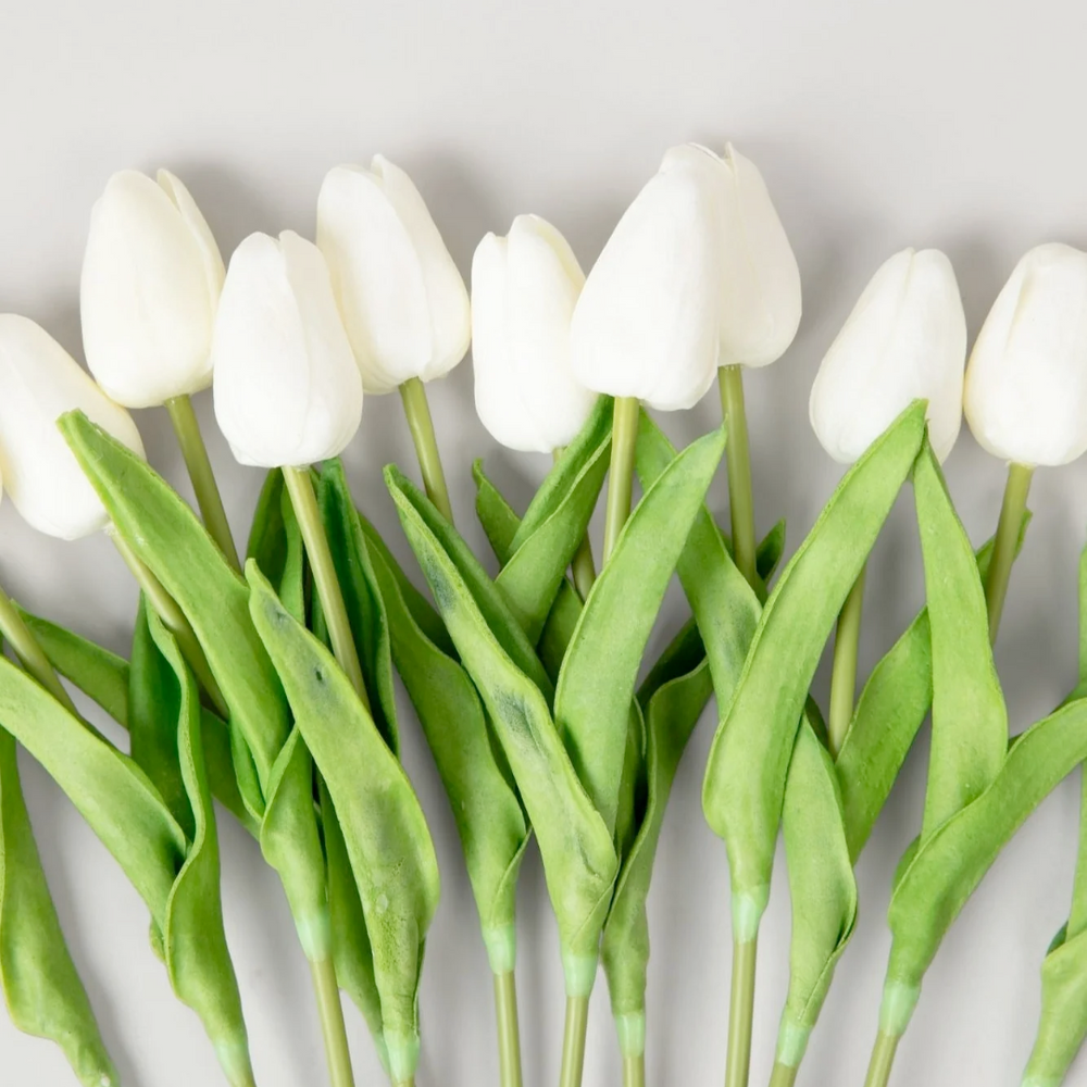 A bundle of white artificial tulips with green leaves, tied with paper bows.