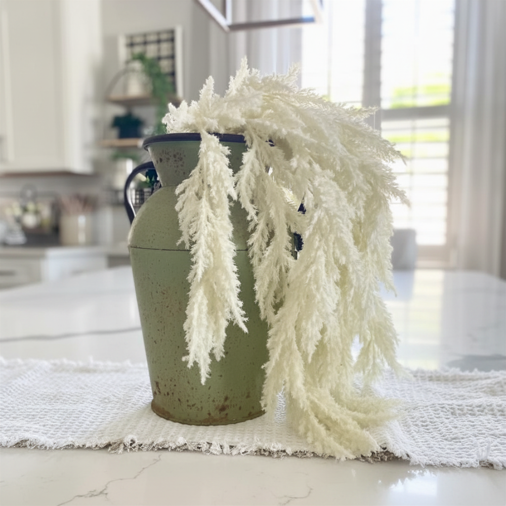 Green vase with white decorative pampas sprays on a table in a kitchen setting