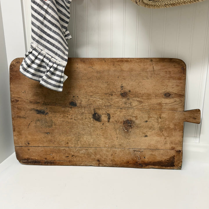 Vintage wooden cutting board with a striped cloth on a white surface and light wood panel background