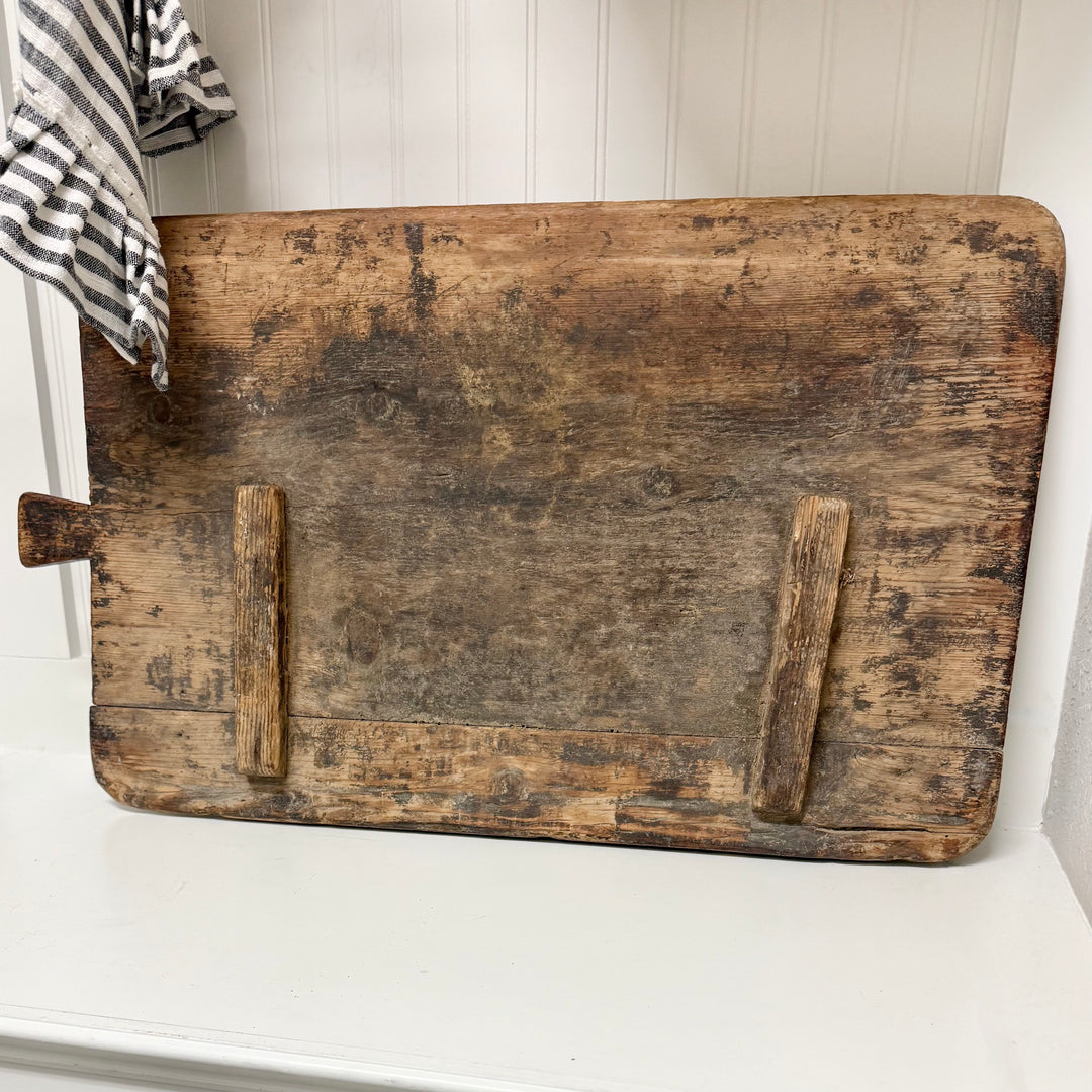 Old wooden cutting board on a white surface with a striped towel in the background