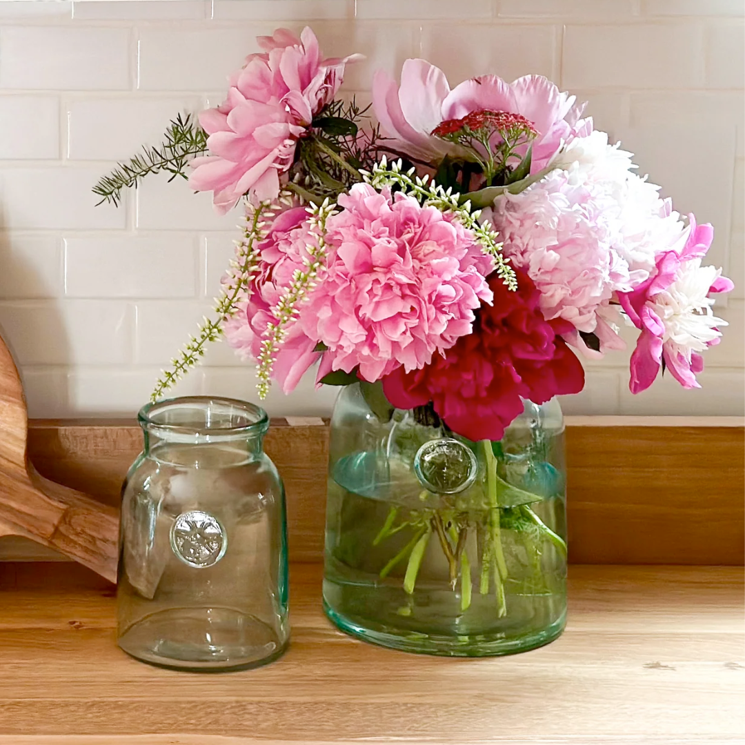 Two glass French mason jars with pink and white flowers on a wooden surface.