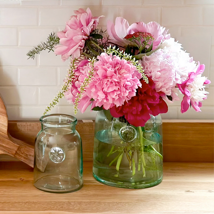 Two glass French mason jars with pink and white flowers on a wooden surface.
