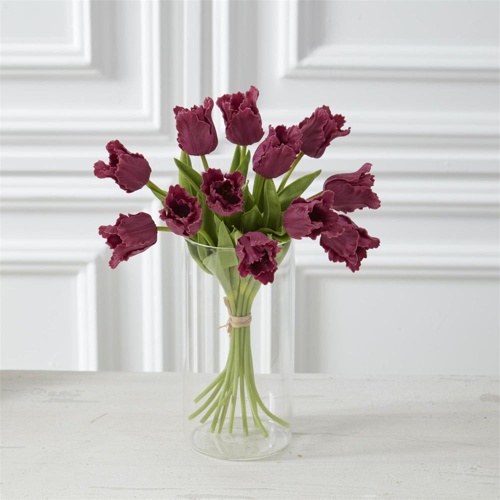 Bouquet of purple tulips in a clear vase against a white paneled wall.