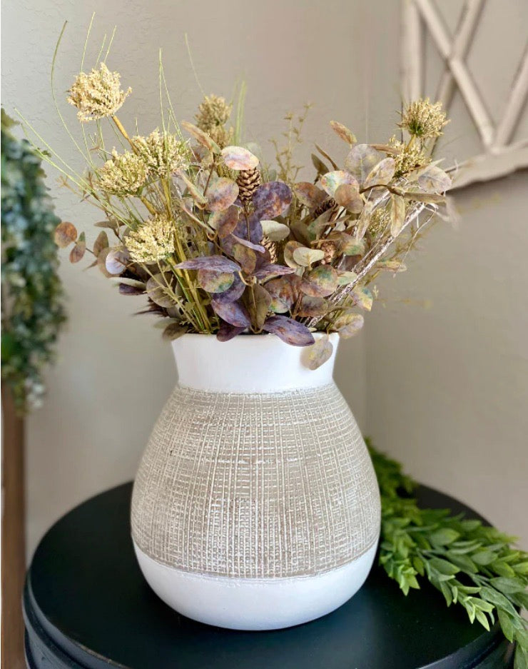 Textured vase with dried flowers on a dark surface