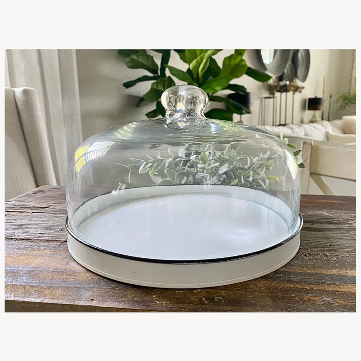 Glass cloche with a white base on a wooden surface.