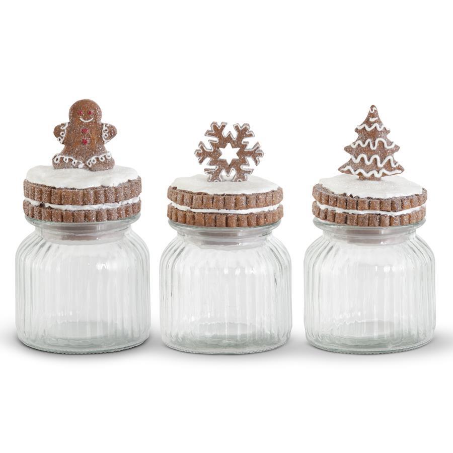 Three glass jars with decorative lids featuring gingerbread men, snowflakes, and Christmas trees on a white background.