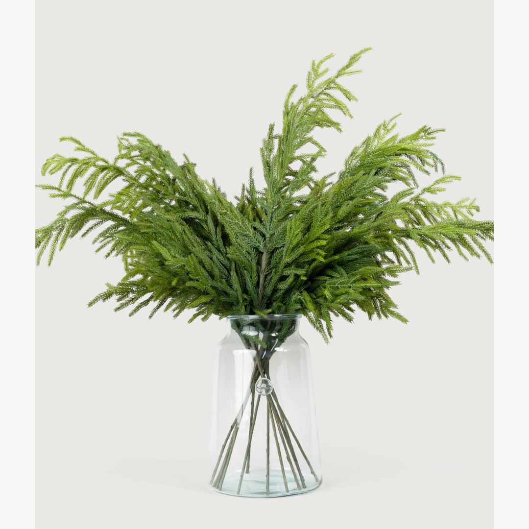 Green artificial Glittered Norfolk Pine Sprays in a clear glass vase on a white background