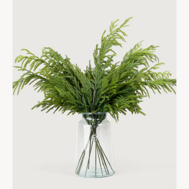 Green artificial Glittered Norfolk Pine Sprays in a clear glass vase on a white background
