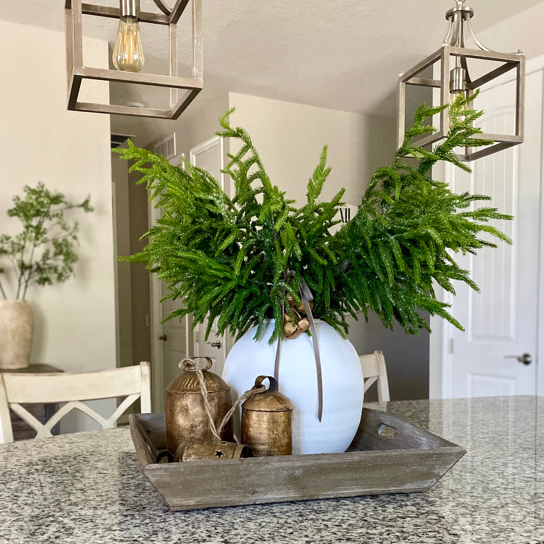 Artificial greenery spray with glittered needles arranged in a decorative vase, set against a cozy home background.