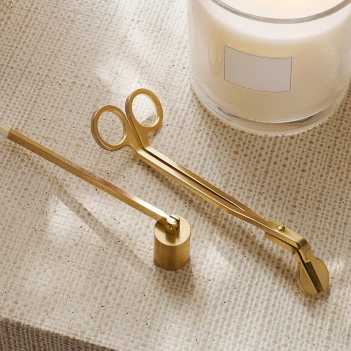 Gold candle snuffer and wick trimmer on a textured surface with a candle in the background