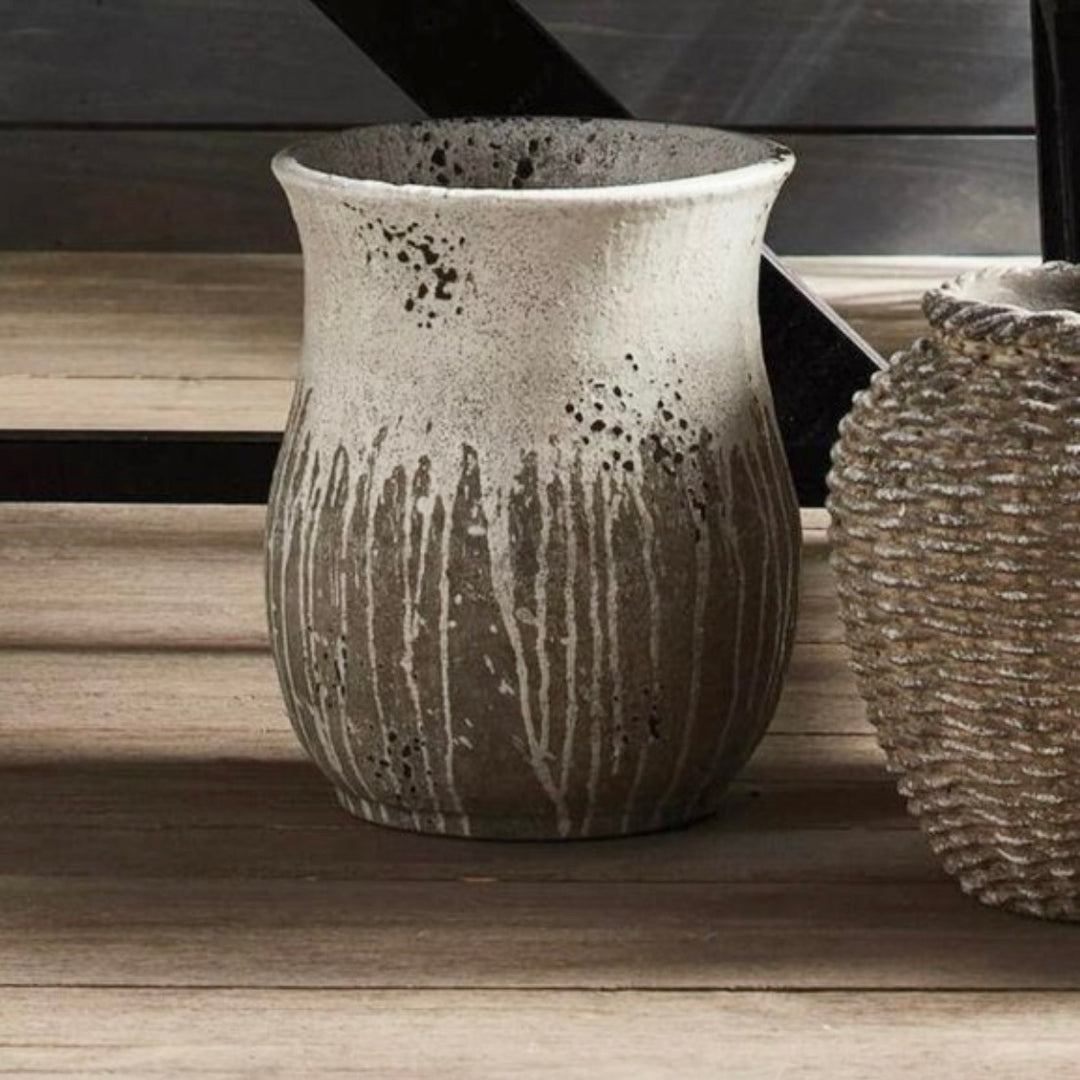 A handcrafted gray and white cement vase with a raw clay texture and thick glaze, displayed on a wooden surface.