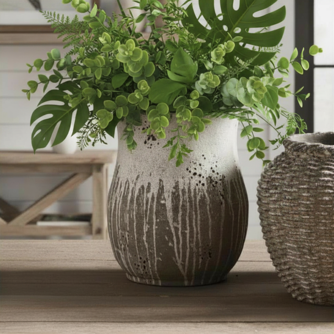 A handcrafted gray and white cement vase with a raw clay texture and thick glaze, displayed on a wooden surface with greenery.