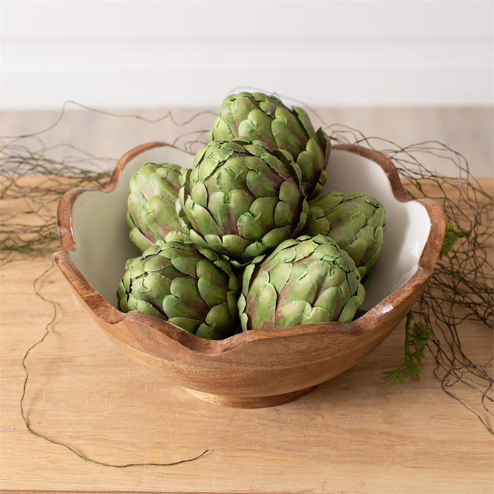 Artificial Green artichokes in a wooden bowl on a wooden surface with a neutral background