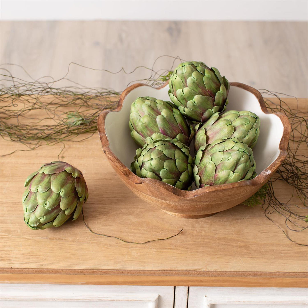 Bowl of faux artichokes on a wooden surface with a natural background
