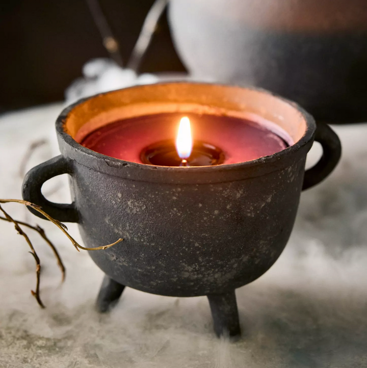 A dark textured aluminum three-legged candle holder with a lit candle inside, surrounded by a misty, atmospheric background.