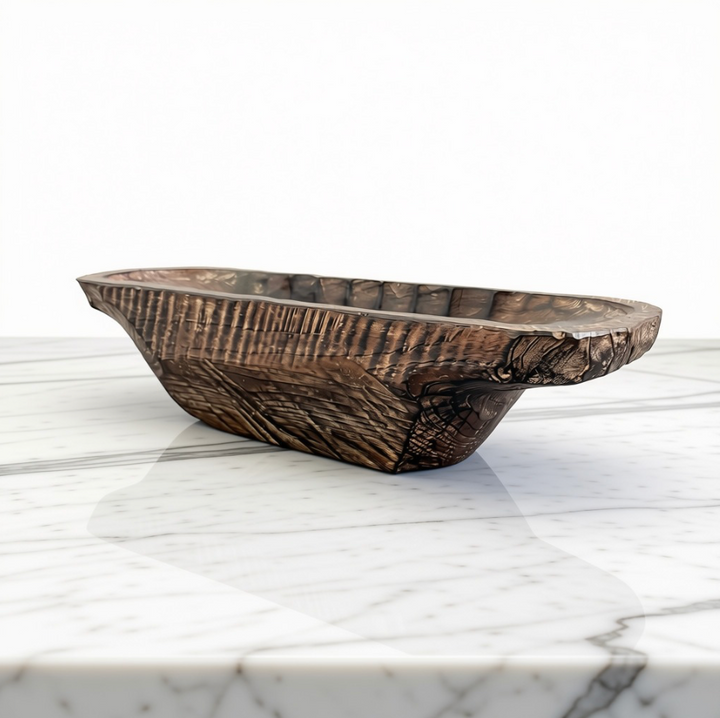 A rustic dark brown carved wooden bowl with a rough, textured surface and natural edge, displayed on a white marble surface against a white background.
