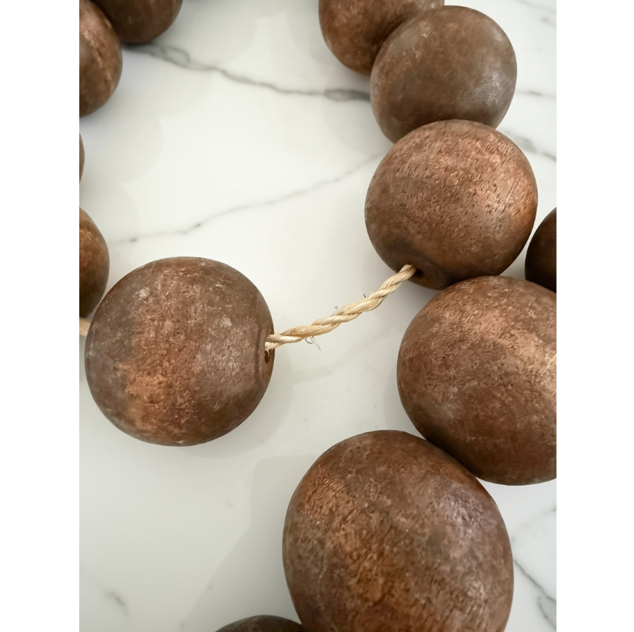 Large round brown wooden beads strung on a natural twine cord, displayed on a white marble surface.
