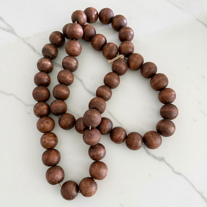 A strand of medium brown wooden beads with natural wood grain, arranged in a loop on a white marble surface.