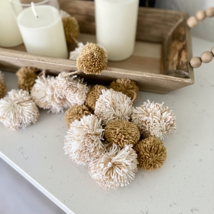 Decorative pom-poms on a surface with candles in the background