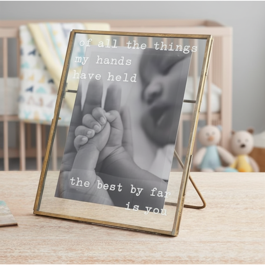Framed photo of a baby's hand held by an adult's hand with text in a nursery setting.