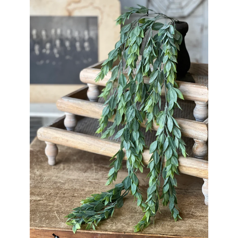 A green leafy garland with cascading branches draped over a rustic wooden tiered stand on a wooden table.