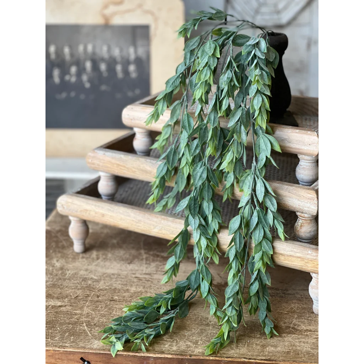 A green leafy garland with cascading branches draped over a rustic wooden tiered stand on a wooden table.