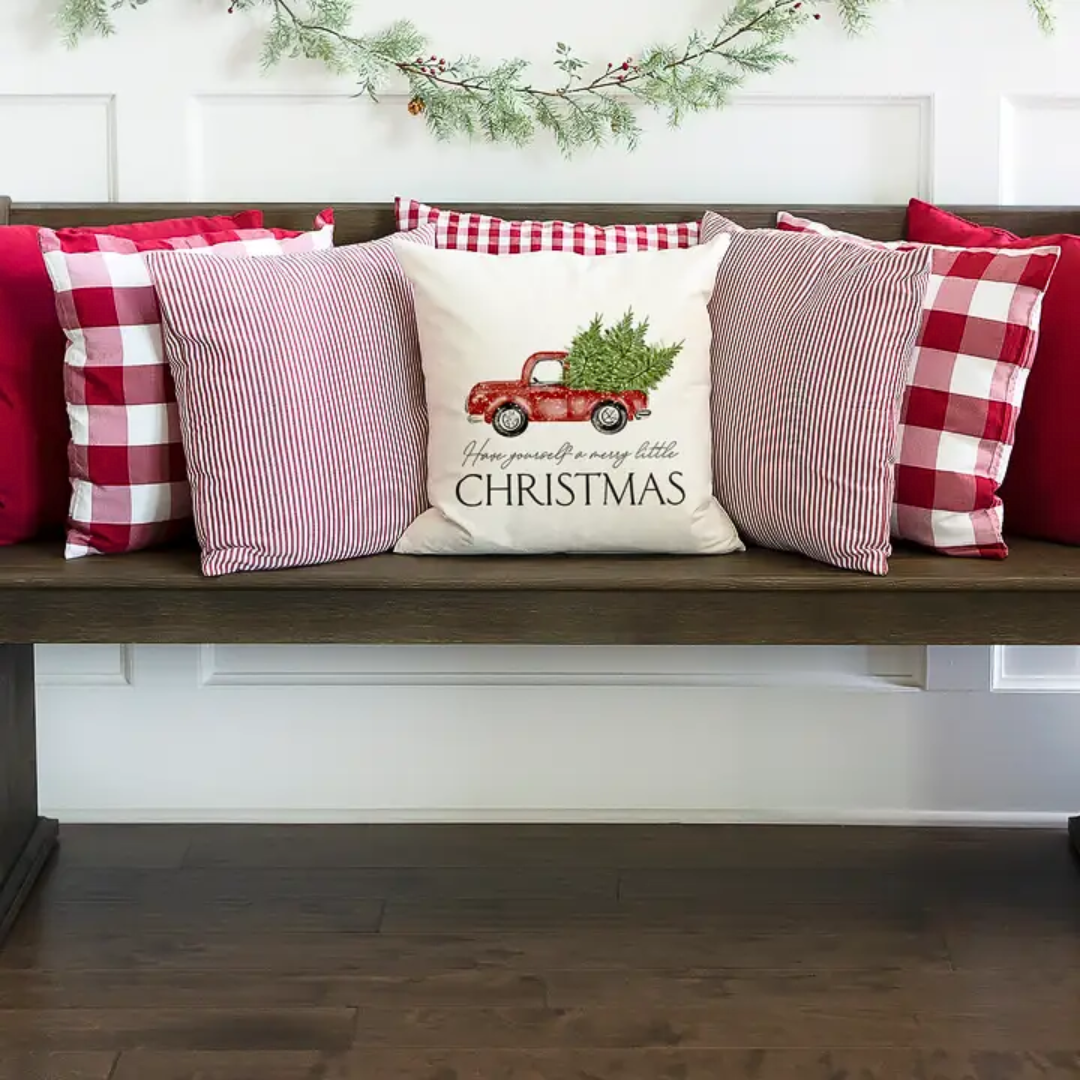 Decorative pillows on a bench with a Christmas-themed pillow featuring a red truck and tree.