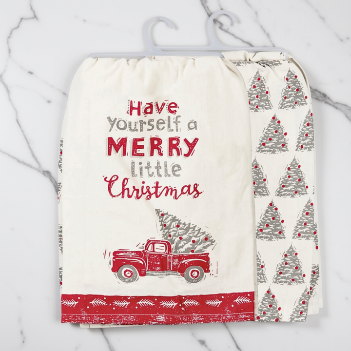 Festive set of two Christmas print tea towels with the text 'Have Yourself a MERRY Little Christmas' in red and gray, a red vintage truck carrying a Christmas tree, and a red patterned border. The coordinating towel shows a repeating gray Christmas tree pattern with red ornaments, set against a white marble background.