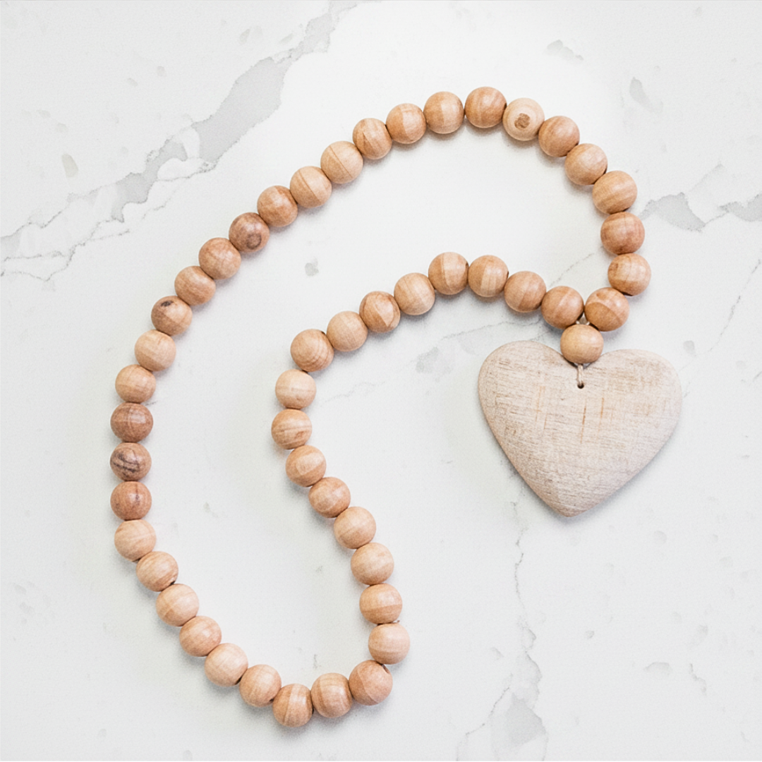 Wooden beaded garland decor with a heart-shaped pendant on a marble surface