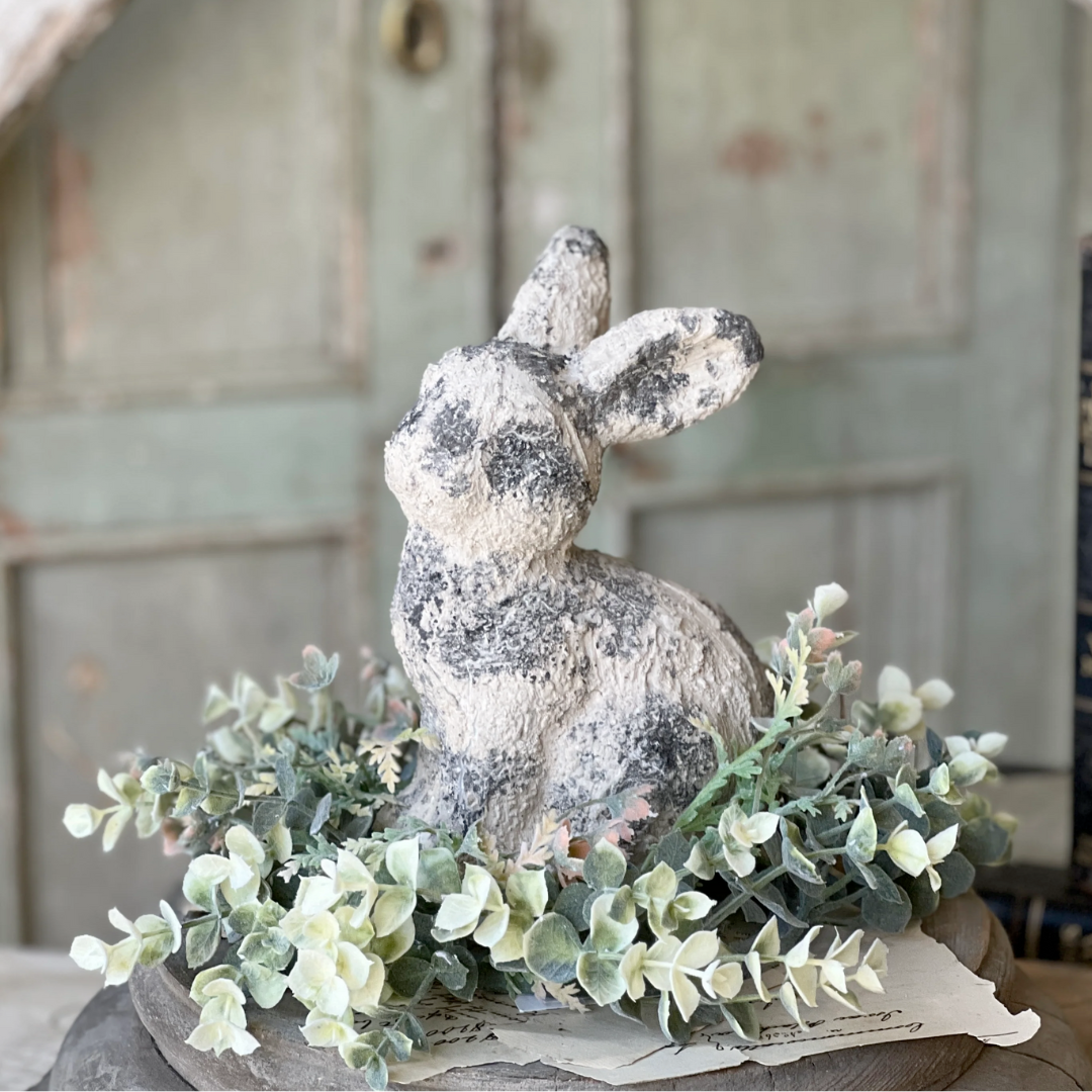 Decorative stone rabbit figurine with greenery on a rustic surface
