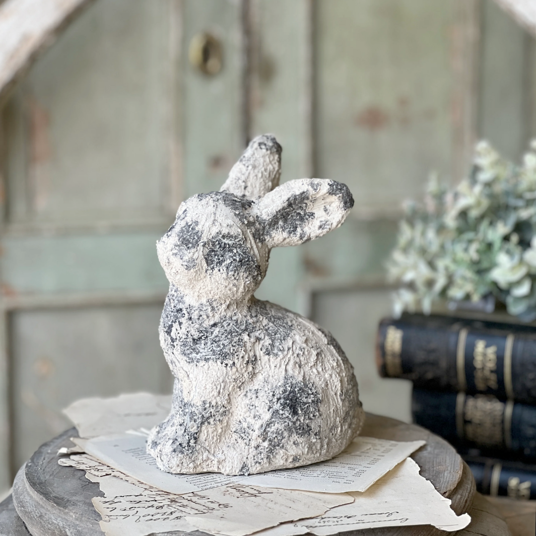 Decorative stone rabbit figurine on a surface with books and papers in the background