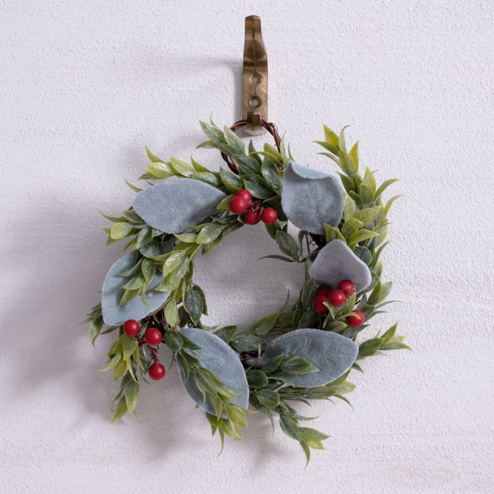 Decorative wreath with green leaves and red berries on a white wall