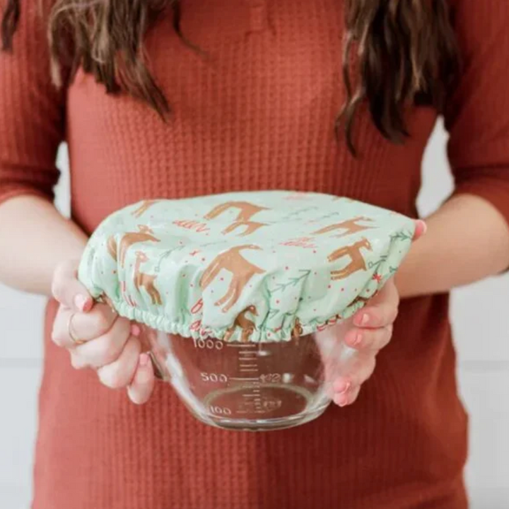 Person holding a glass measuring cup with a green fabric bowl cover featuring a deer pattern