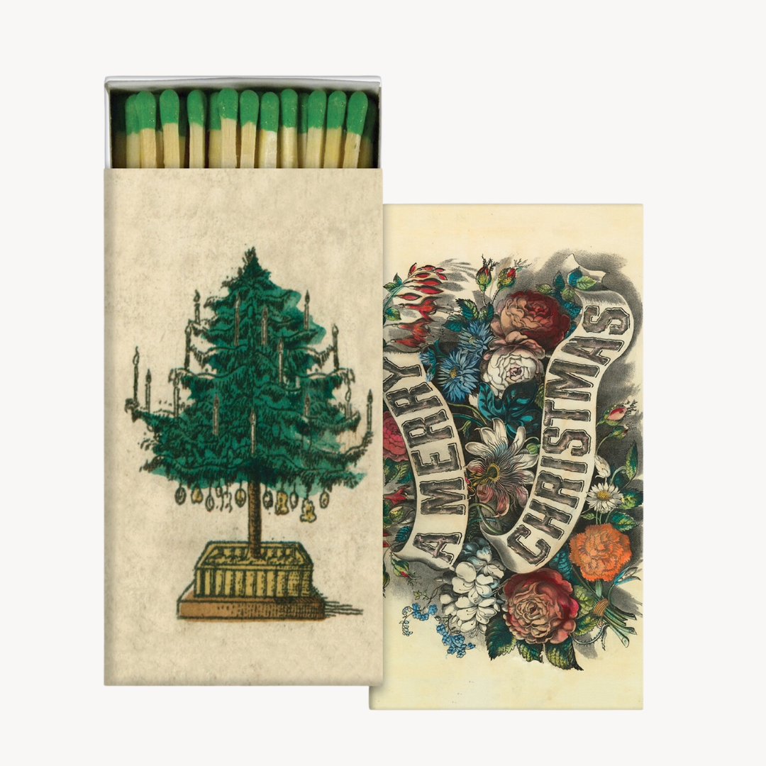 Two matchboxes with Christmas-themed designs. One shows a green Christmas tree with ornaments and the text 'Merry Christmas', and the other has a colorful floral and festive decoration design.