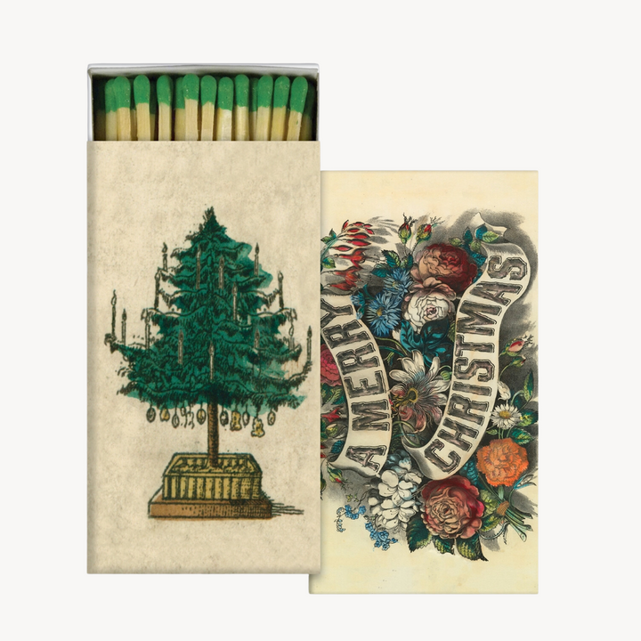 Two matchboxes with Christmas-themed designs. One shows a green Christmas tree with ornaments and the text 'Merry Christmas', and the other has a colorful floral and festive decoration design.