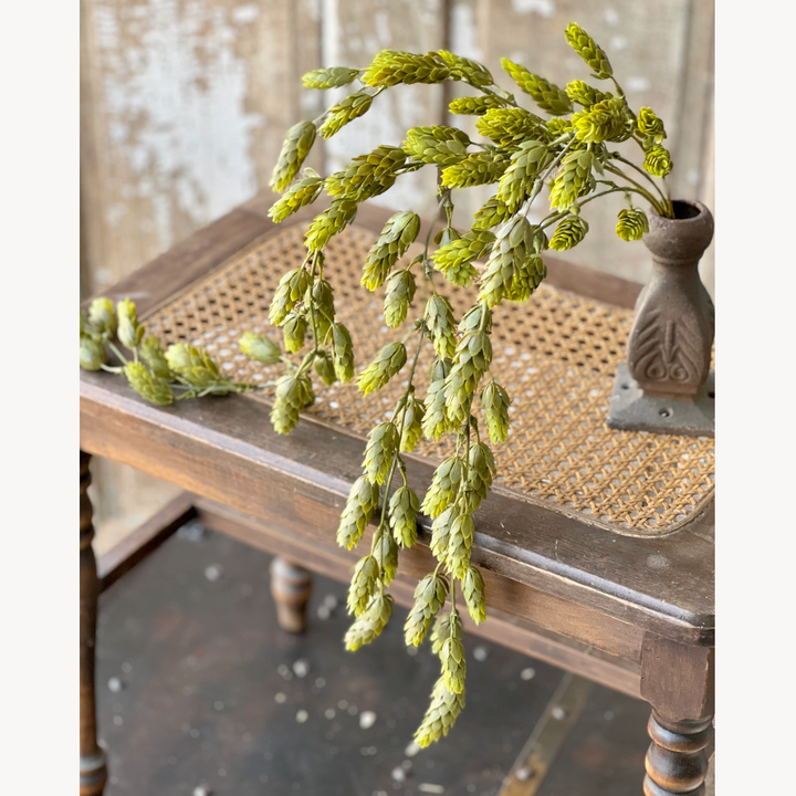 A faux greenery decoration hanging over the edge of a wooden table, with a rustic vase in the background.