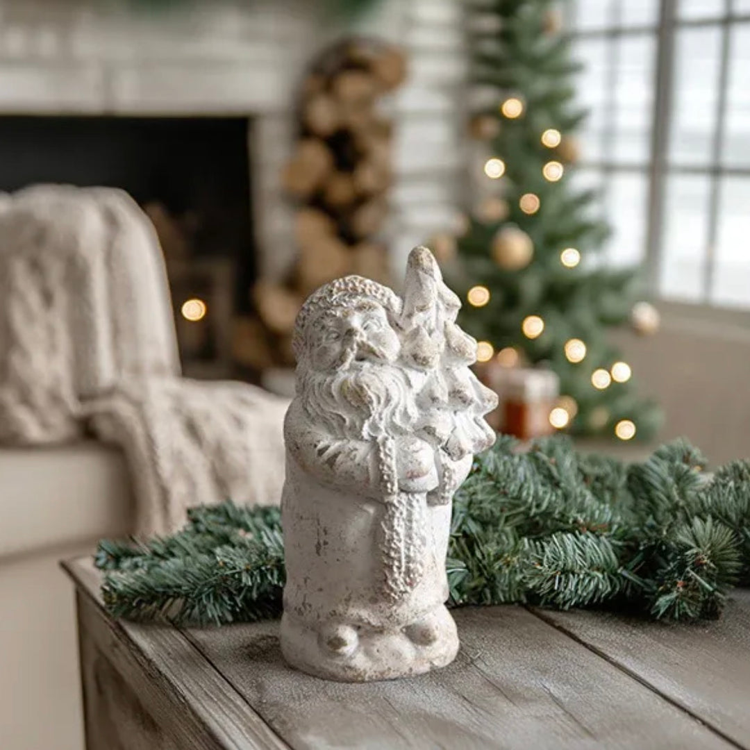 Decorative Santa Claus figure on a wooden surface with a Christmas tree and fireplace in the background.
