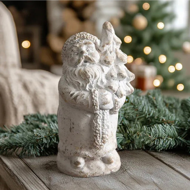 Decorative stone Santa Claus figure with a Christmas tree on a wooden surface with festive lights in the background.