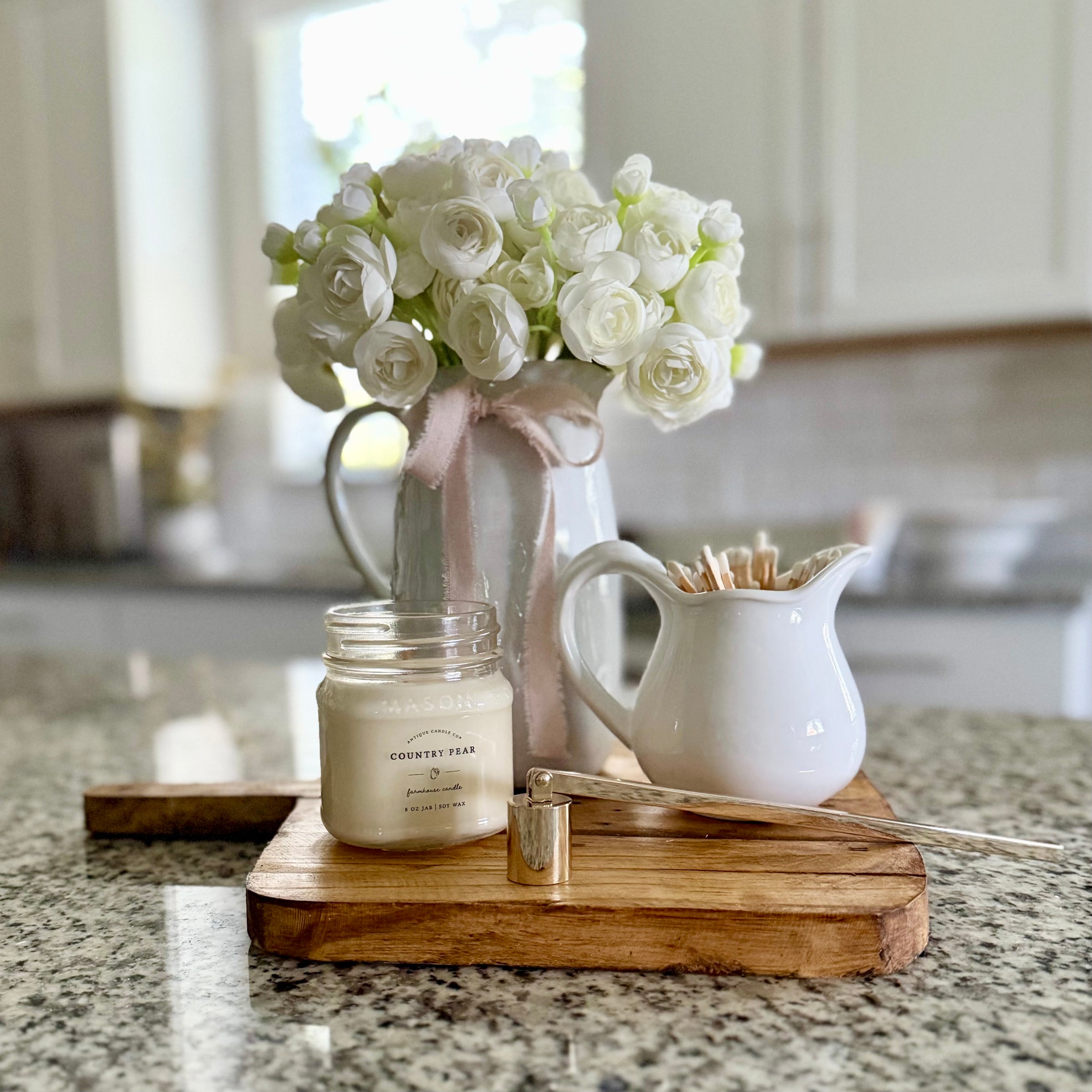 Decorative setup on a kitchen counter with flowers, candle, and small pitcher.