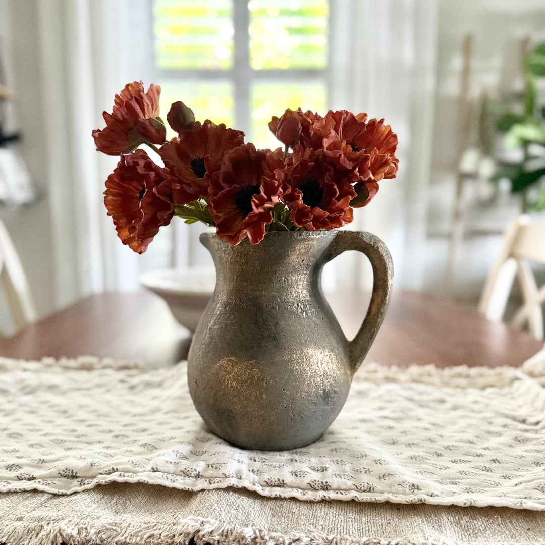 Decorative distressed terracotta vase with red flowers on a floral table runner