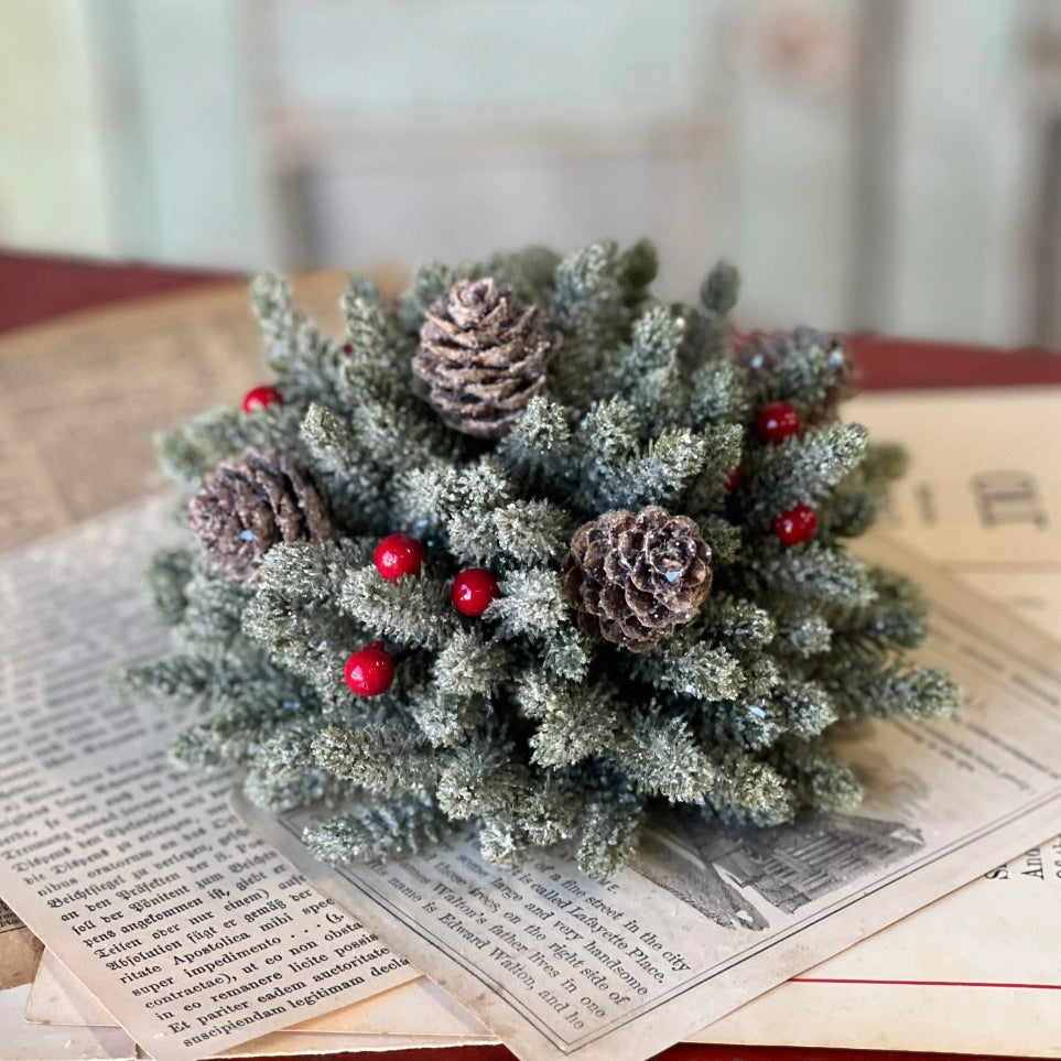 A decorative half sphere featuring icy pine branches with red berries and a silver sparkle finish, placed on a newspaper background.