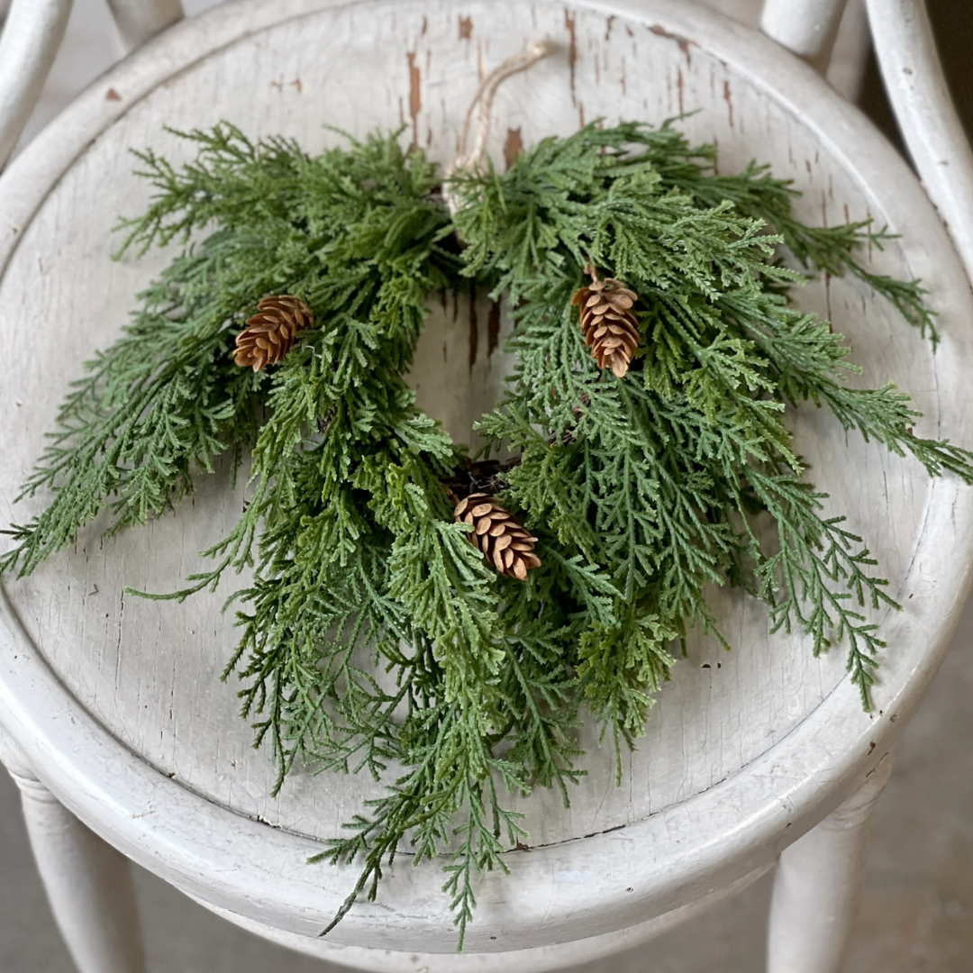 Artificial Green Christmas cedar wreath with pine cones on a white wooden stool