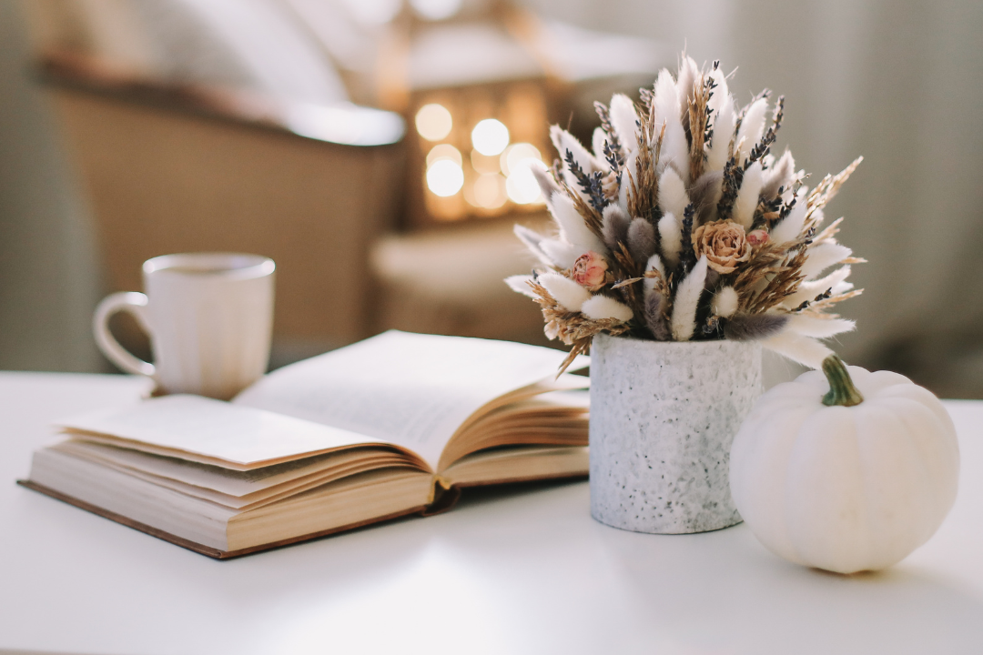 Open book, cup, and decorative arrangement on a table with a blurred background